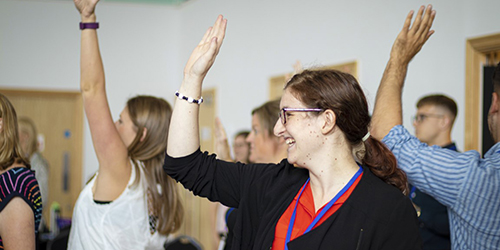 Room of teachers with hands up, smiling